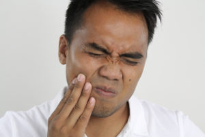 Man winces in pain from a tooth and will need an emergency dentist appointment to help relieve the discomfort. 