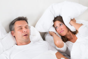 Image of woman covering her ears with a pillow because husband snores which is a symptom of sleep apnea.